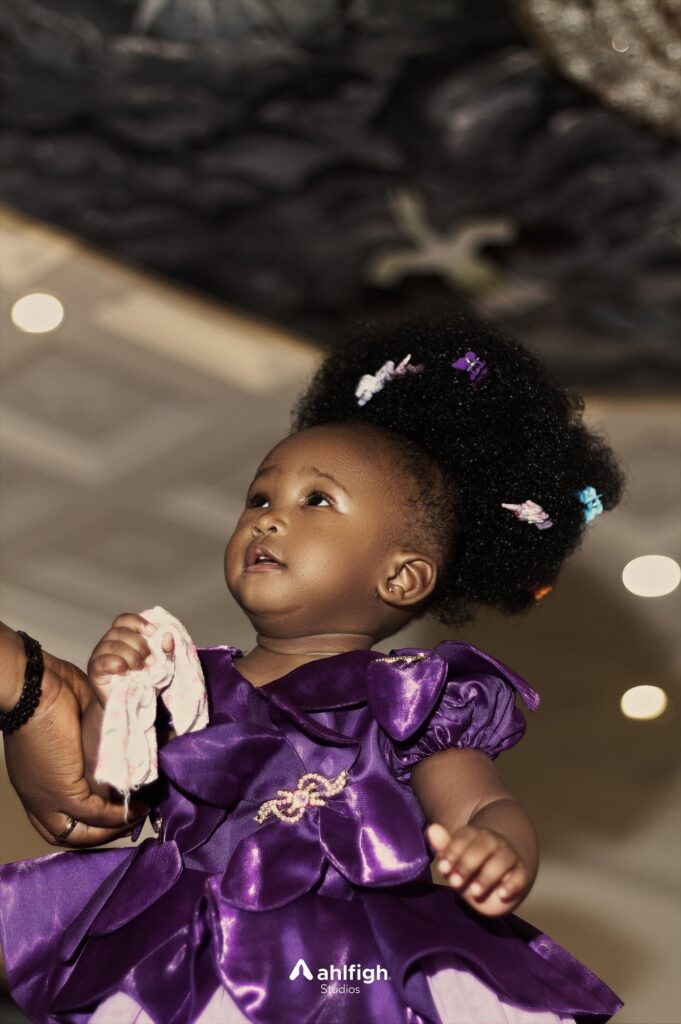 Virtue in a purple party dress looks up, clips in her curls